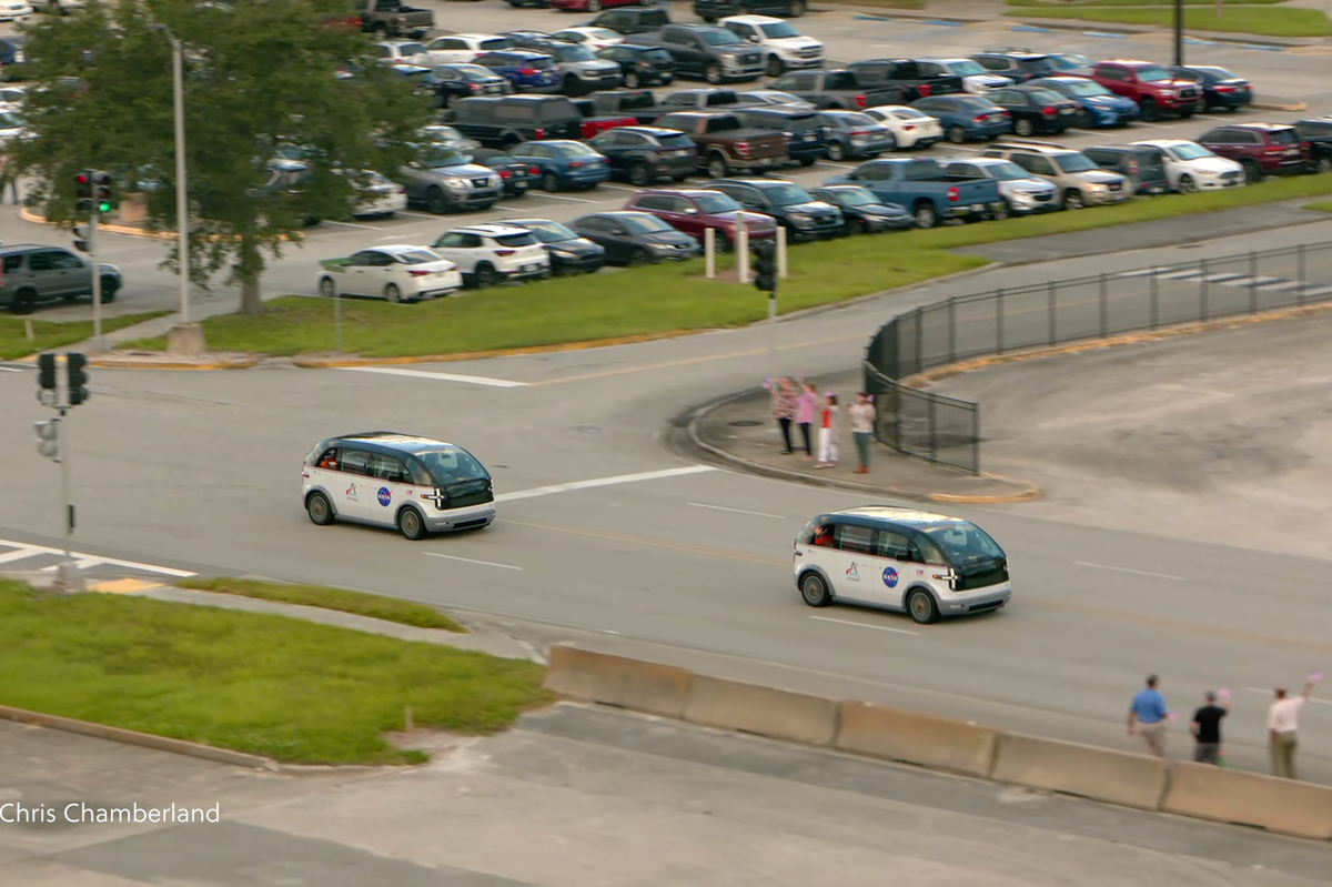 Two Canoo-made \u201cCrew Transportation Vehicles\u201d drive down a Florida highway while bystanders wave at them.