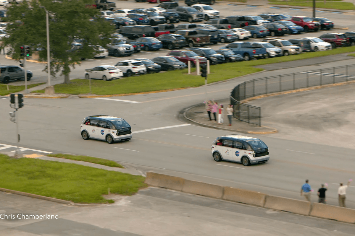 Two Canoo-made \u201cCrew Transportation Vehicles\u201d drive down a Florida highway while bystanders wave at them.