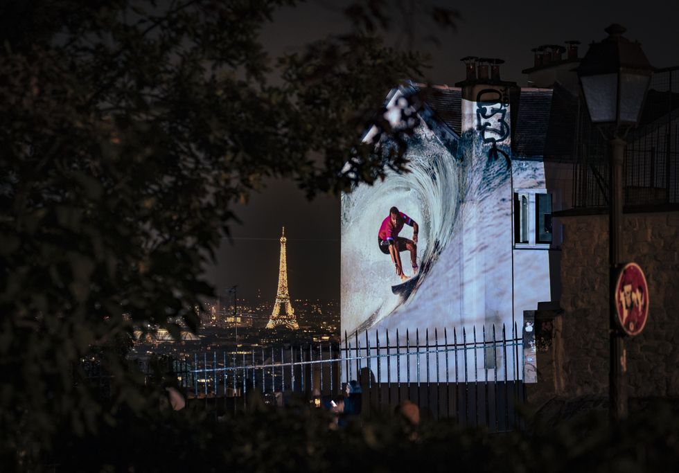 An image of French athlete Joan Duru surfing at Teahupo'o, projected on a wall in Paris\u2019 Montmartre.