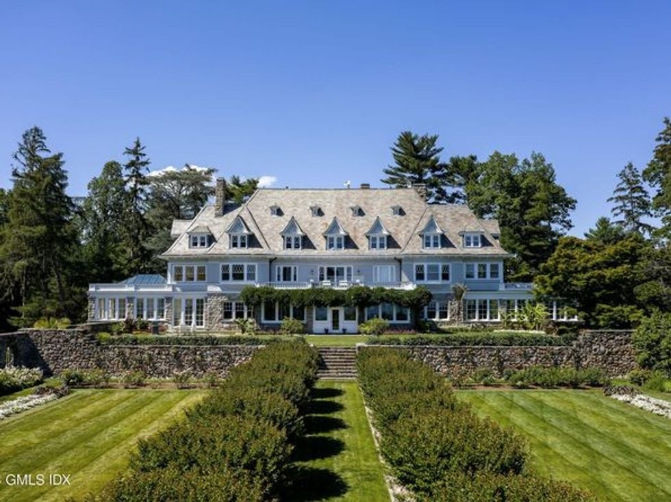 A light-colored, expansive three-story house behind a well-manicured lawn.