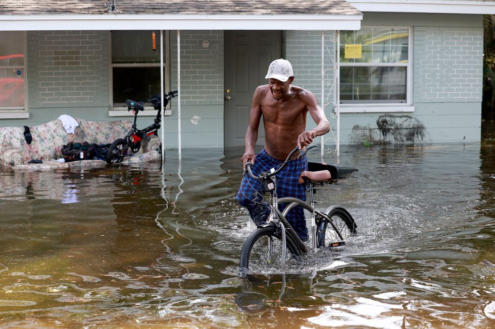 A man walking his bike through floodwaters.